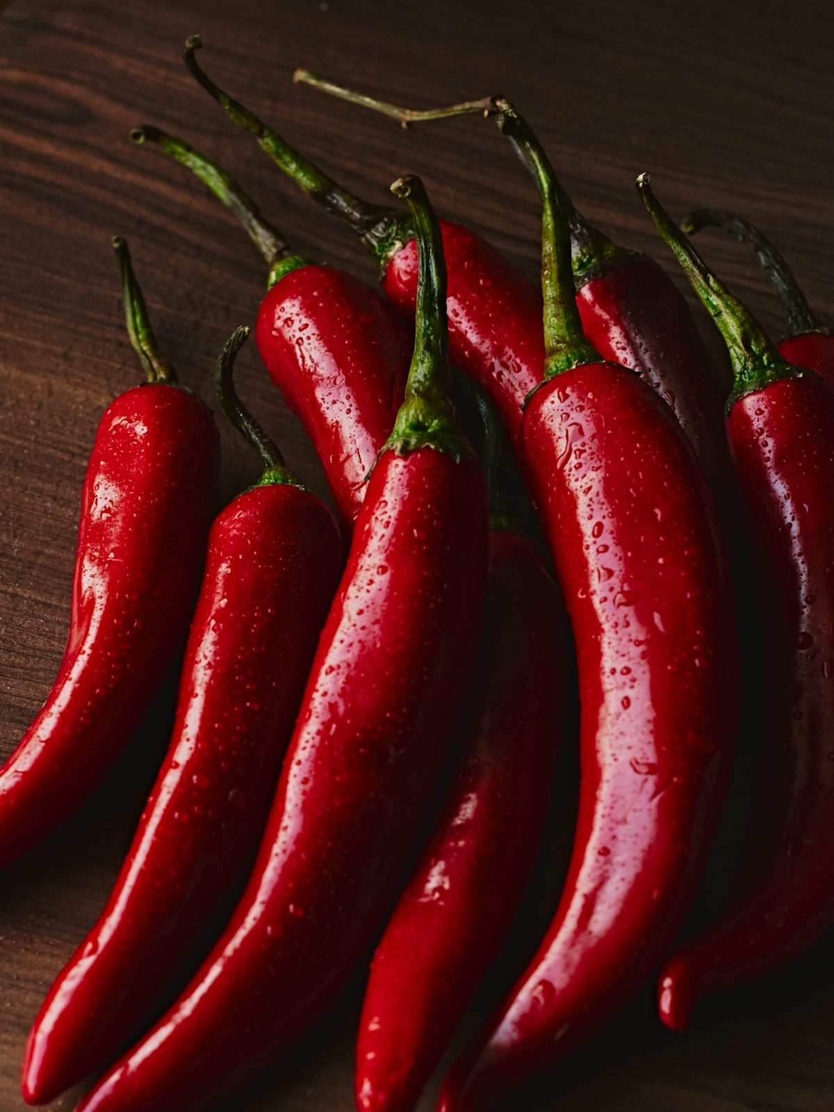 Ripe, red chili peppers arranged on a wooden surface.