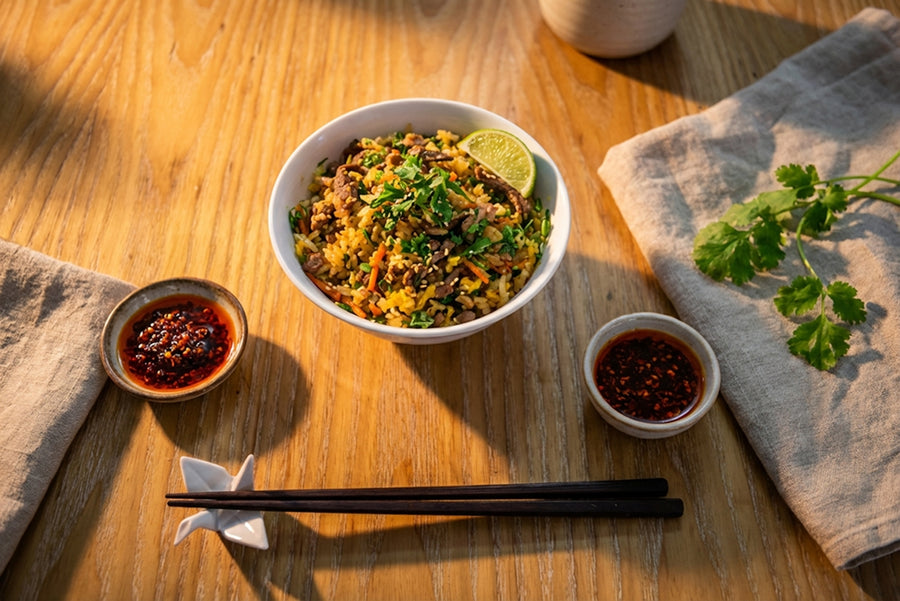 A bowl of rice with toppings, chili oil, and chopsticks.